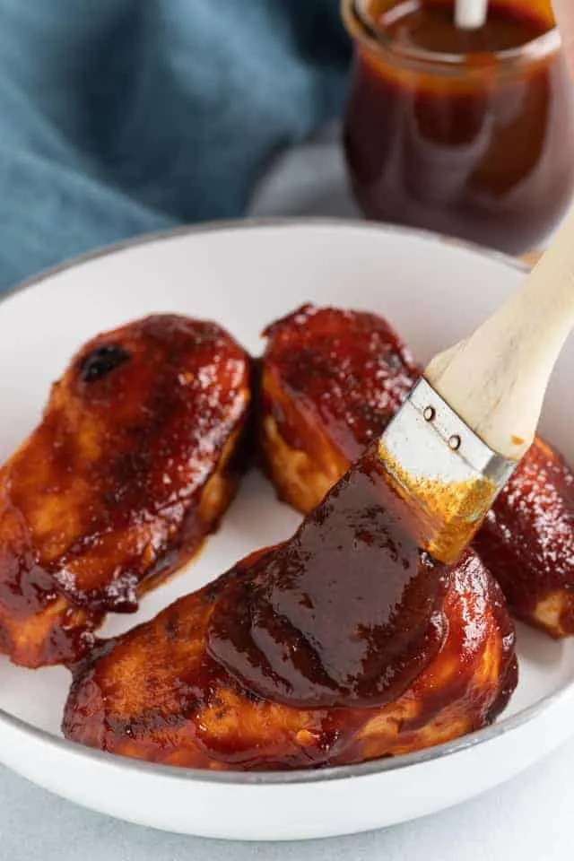 Jack Daniels sauce being brushed over chicken breasts in a white pan