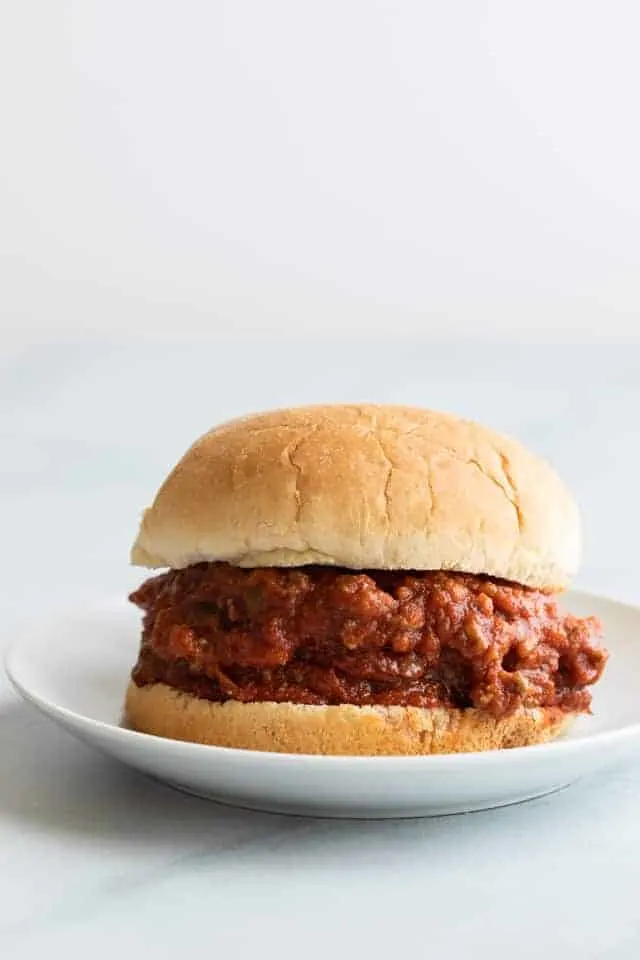 Sloppy joe sauce on a bun set on a white plate