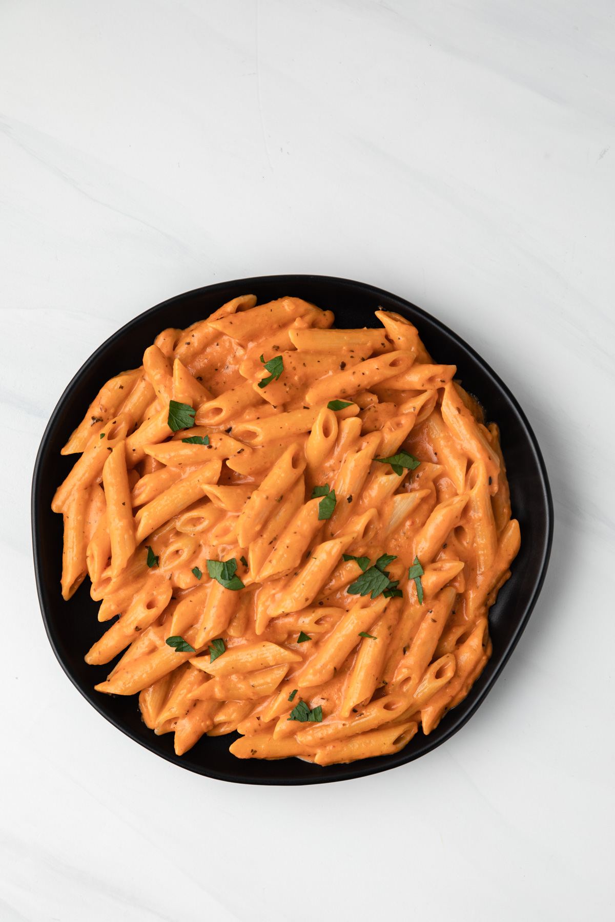 Pink sauce and pasta on a black plate.