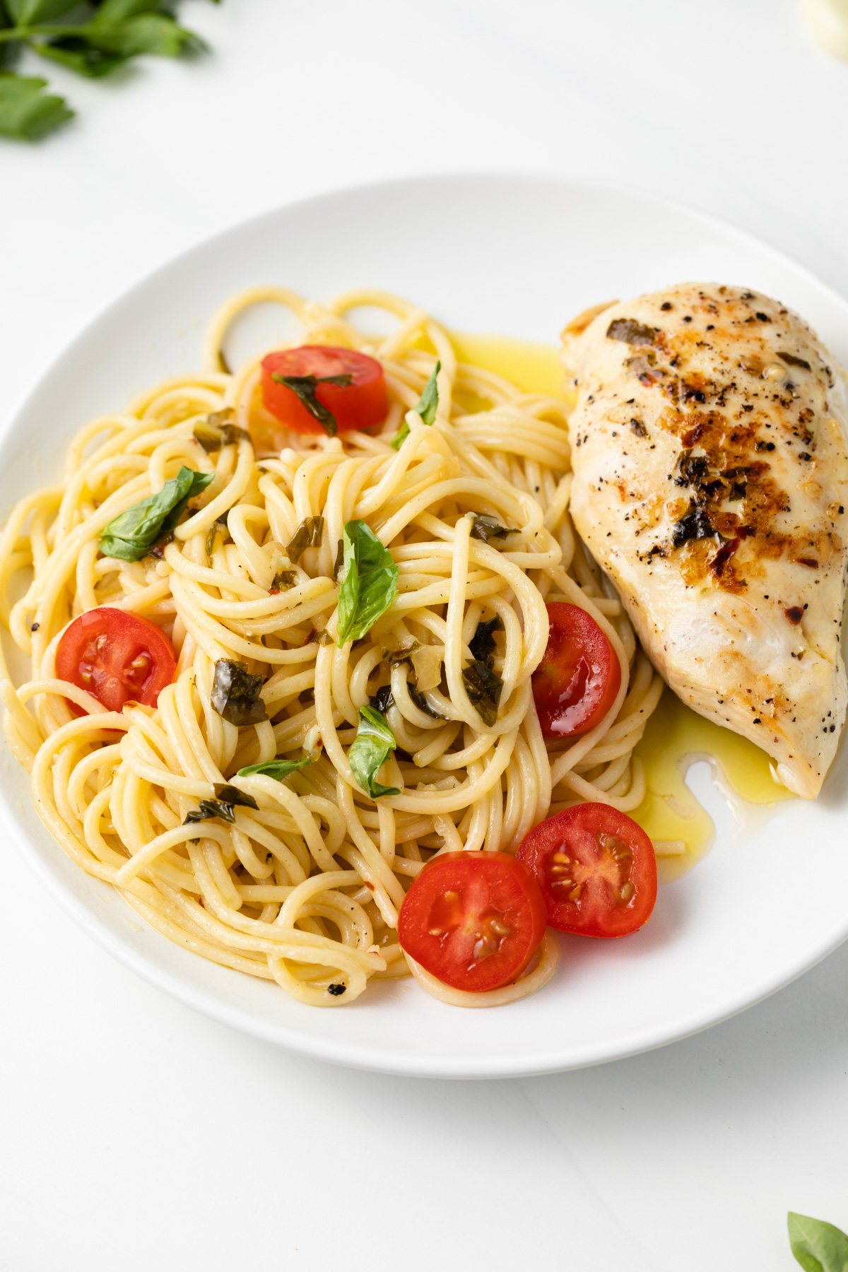 Pasta and chicken with tomatoes and basil on white plate.