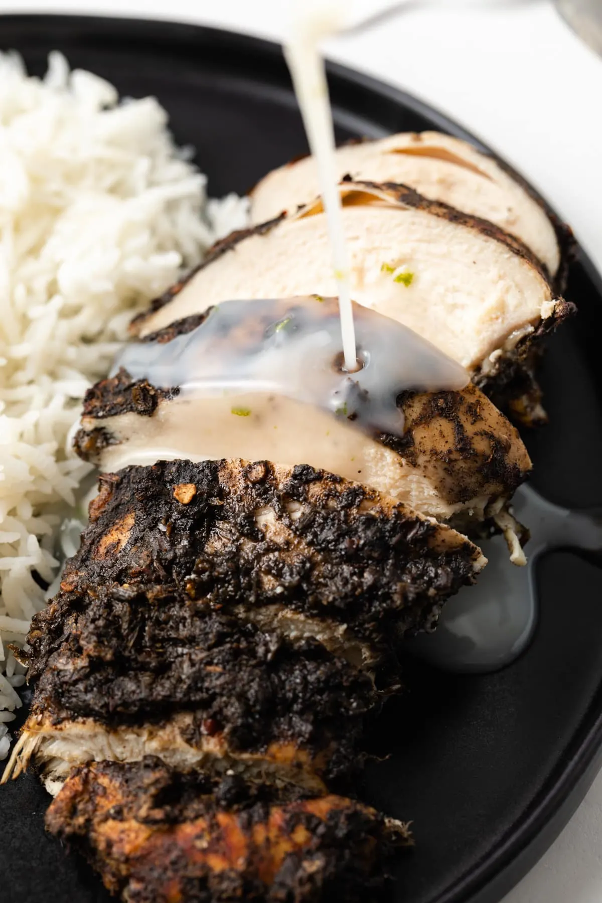 Coconut cream sauce being poured over jerk chicken.