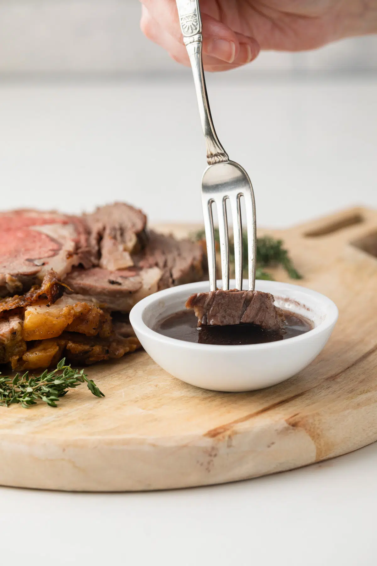 Prime rib being dipped into au jus sauce.