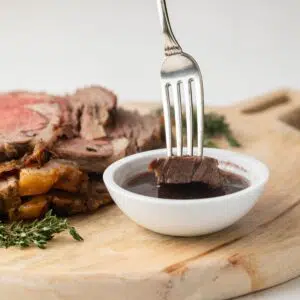 Prime rib being dipped into au jus sauce.