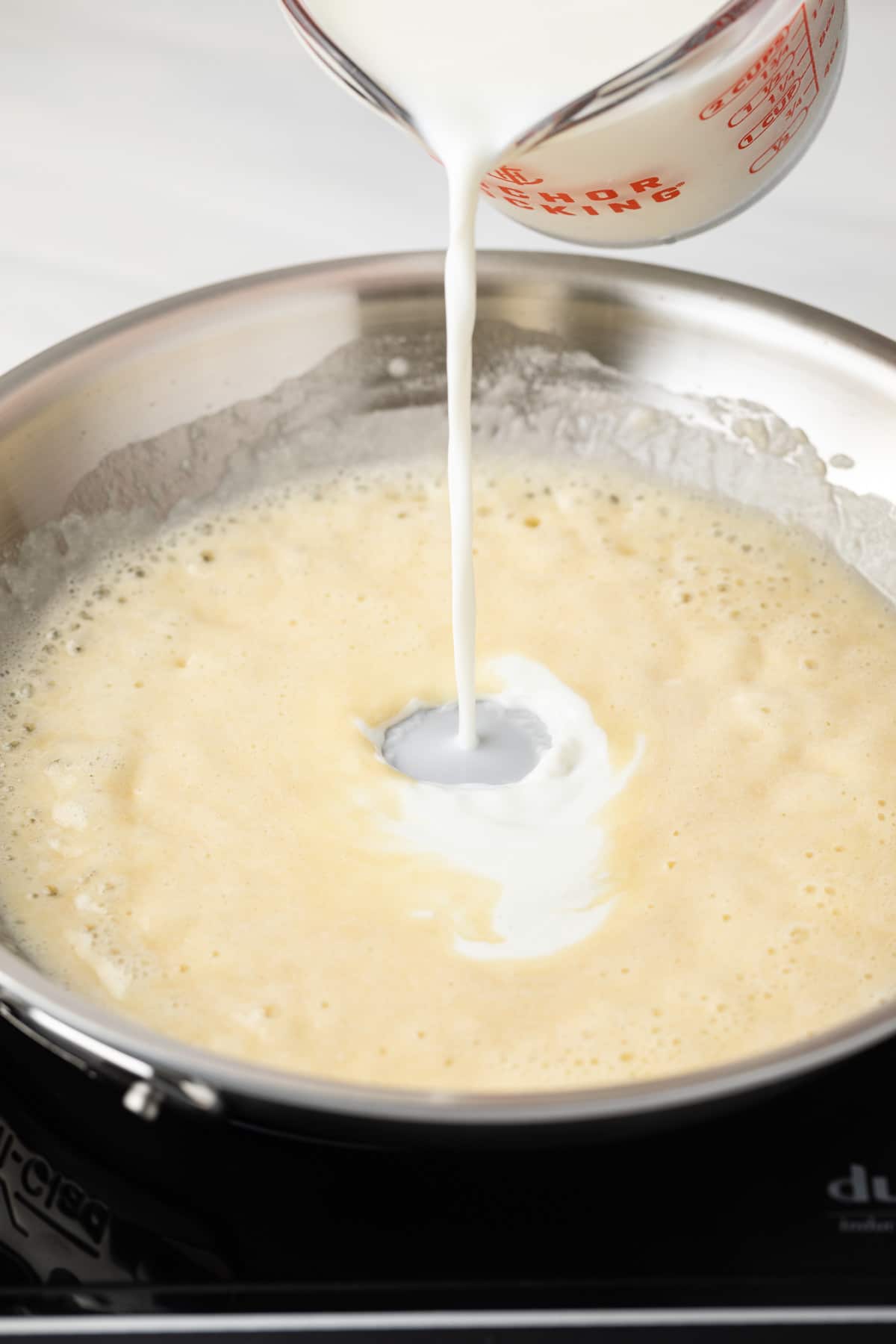 Adding milk to roux in pan.