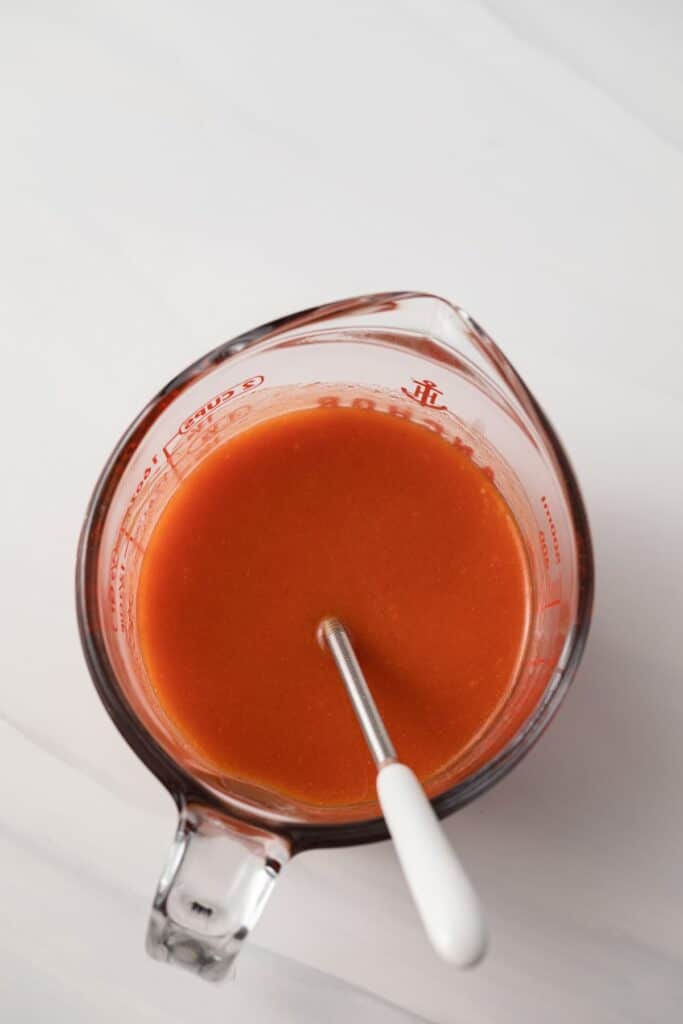 Buffalo sauce in a liquid measuring cup.