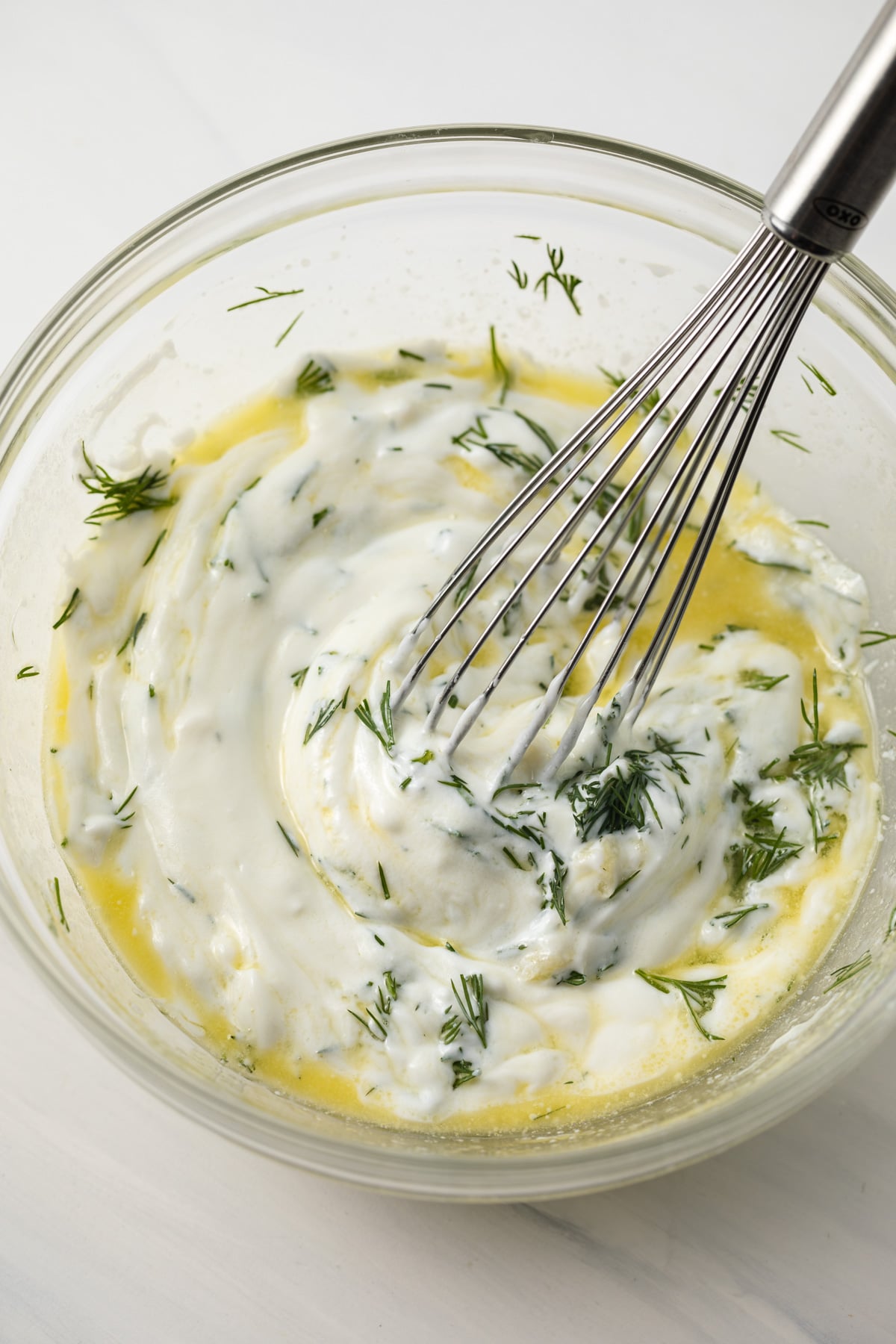 Yogurt, dill, olive oil mixed in glass bowl.