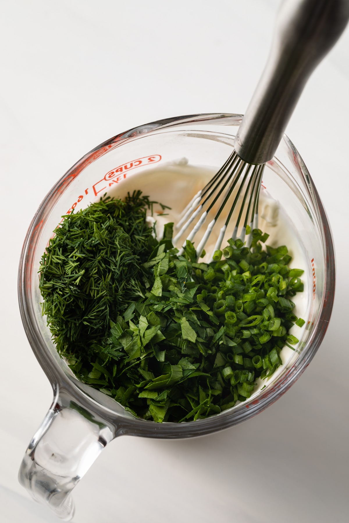Fresh herbs in glass measuring cup with mayonnaise and sour cream.