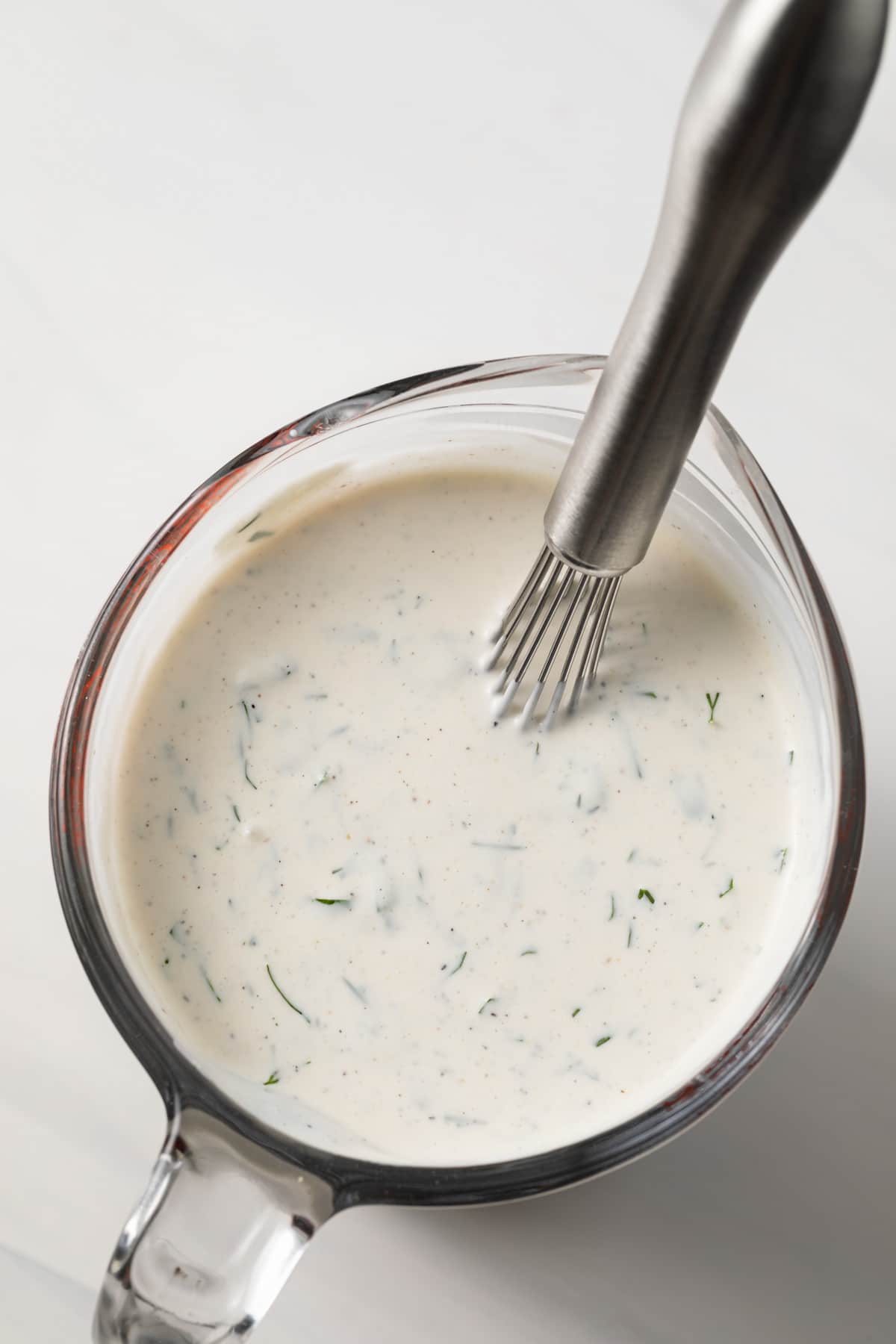 Ranch dressing in glass measuring cup.