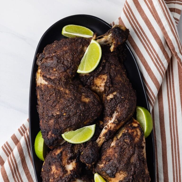 Jamaican jerk chicken on a plate with lime wedges.