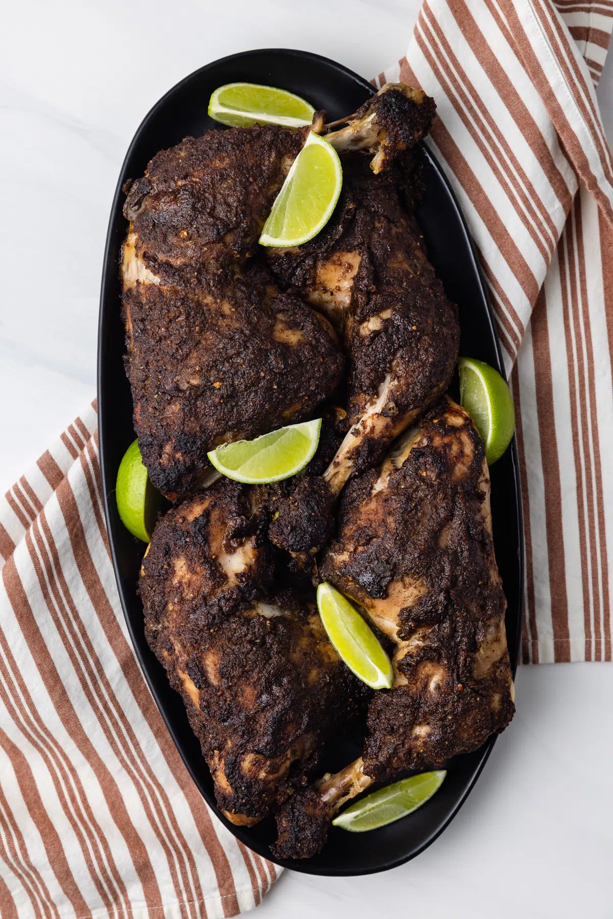 Jamaican jerk chicken on a plate with lime wedges.