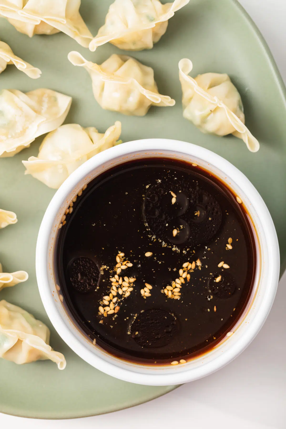 Dim sum dipping sauce in white bowl with dumplings on a plate.