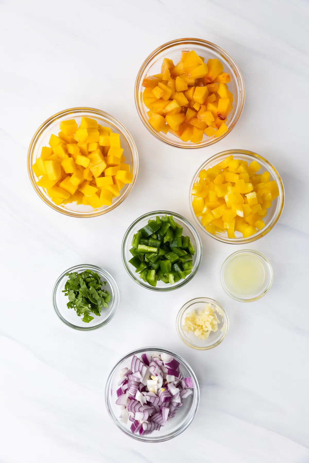 Ingredients for peach mango salsa in glass bowls.