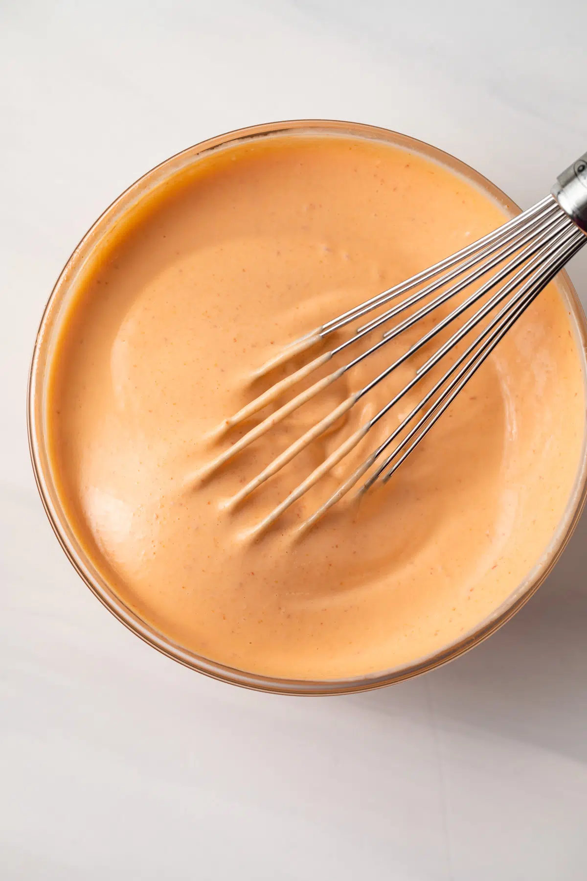 Sriracha mayo in glass bowl with whisk.