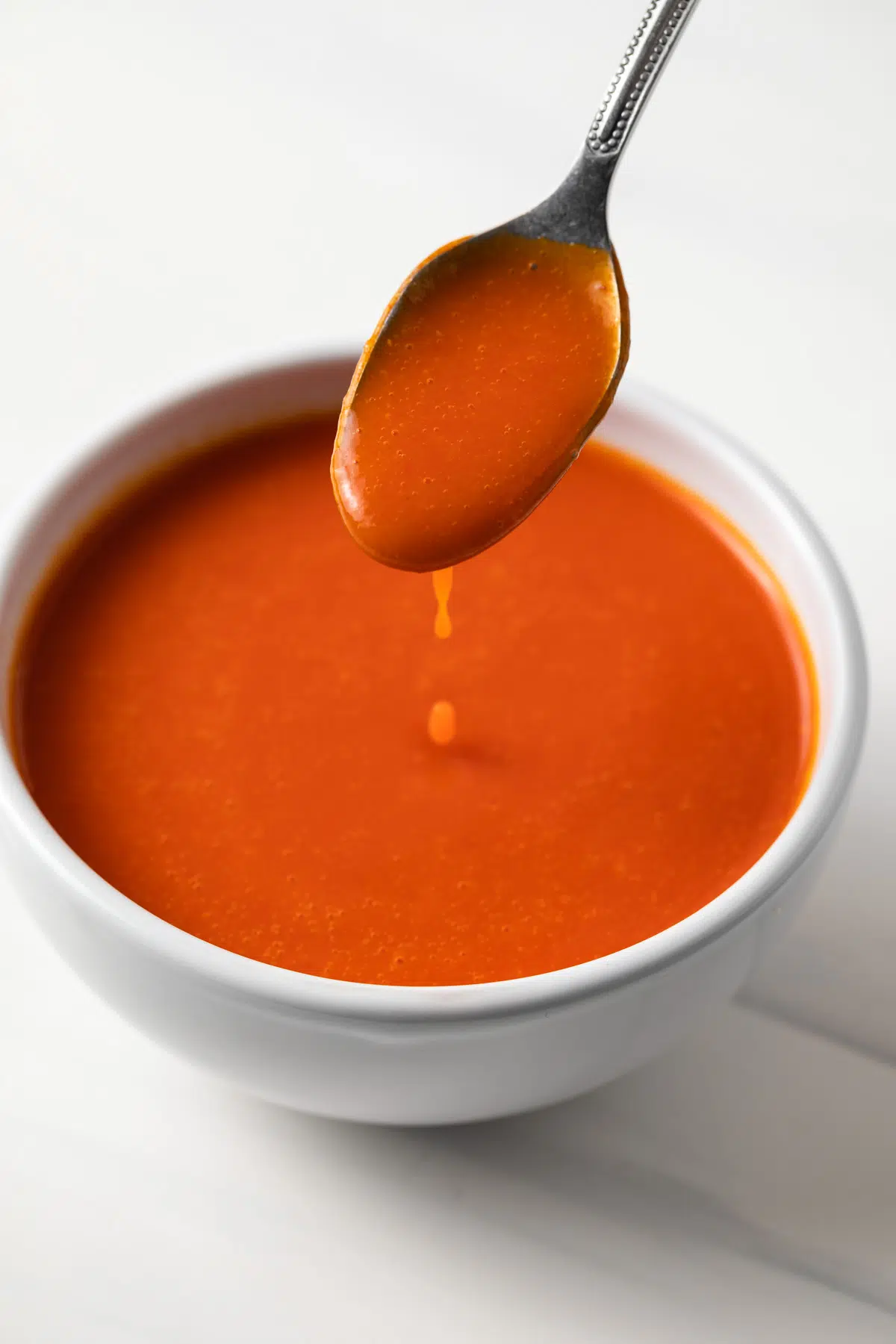 Cayenne pepper hot sauce dripping off a spoon in a white bowl.