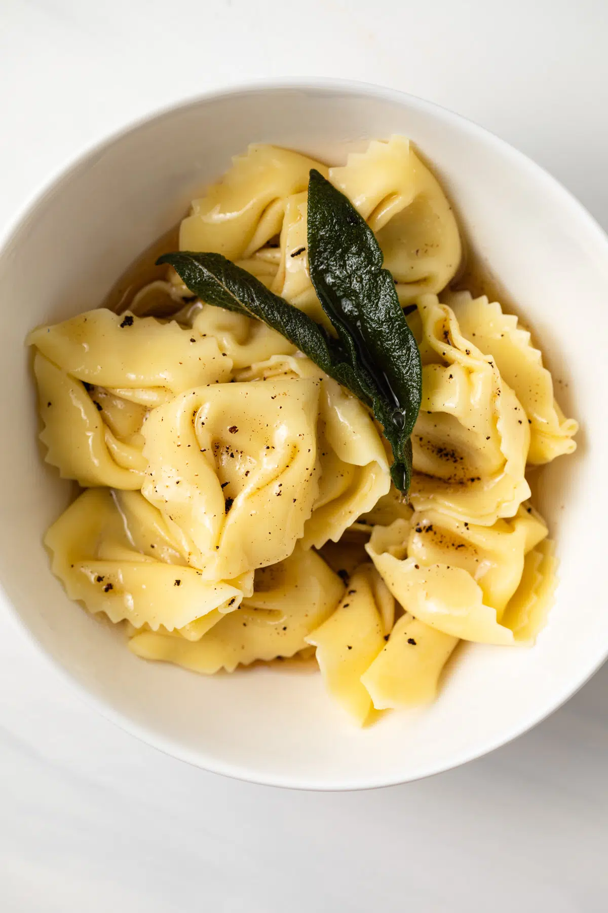 Tortellini with sage butter sauce in a white bowl.