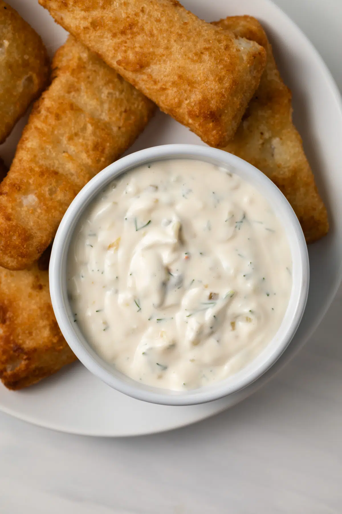 Tartar sauce in white bowl with fish fillets.