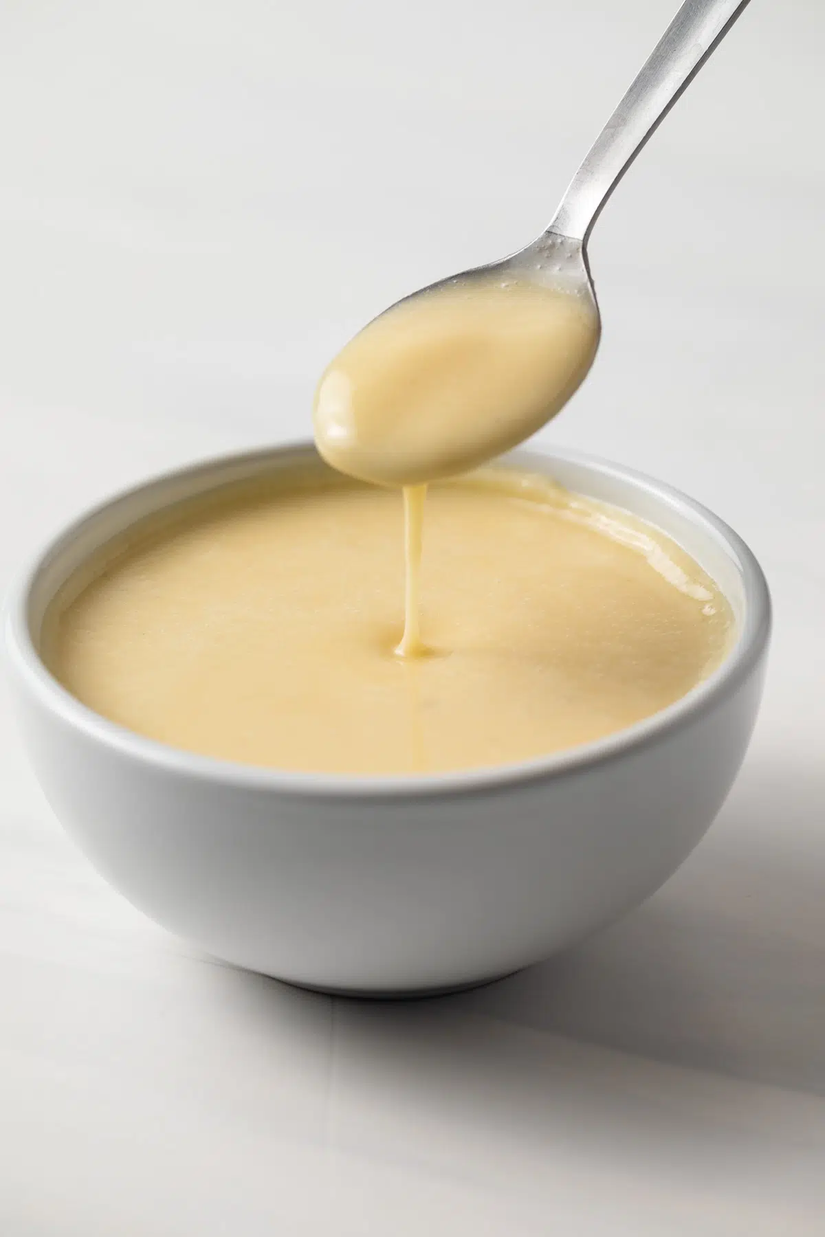 Beurre blanc sauce in white bowl with spoon.