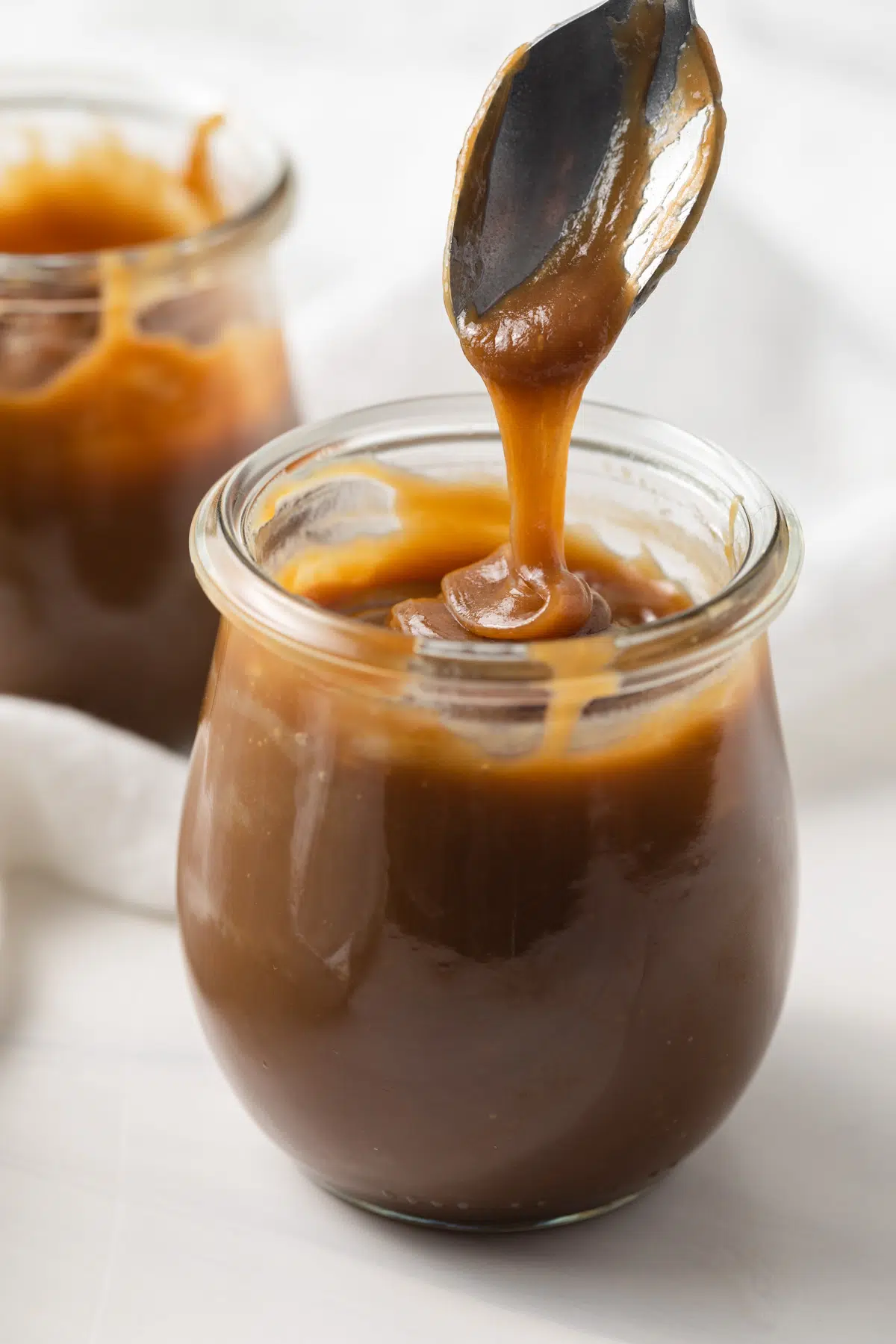 Butterscotch sauce drizzled off spoon into jar.