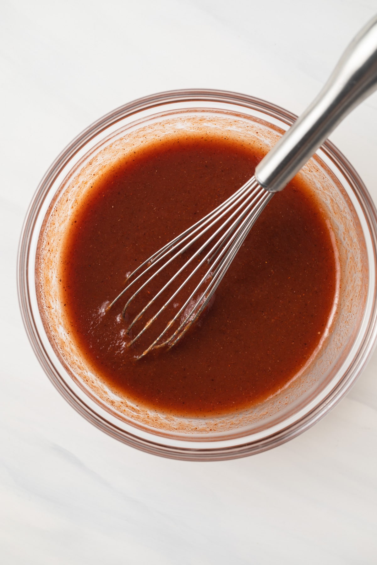 Chili sauce in glass bowl with whisk.