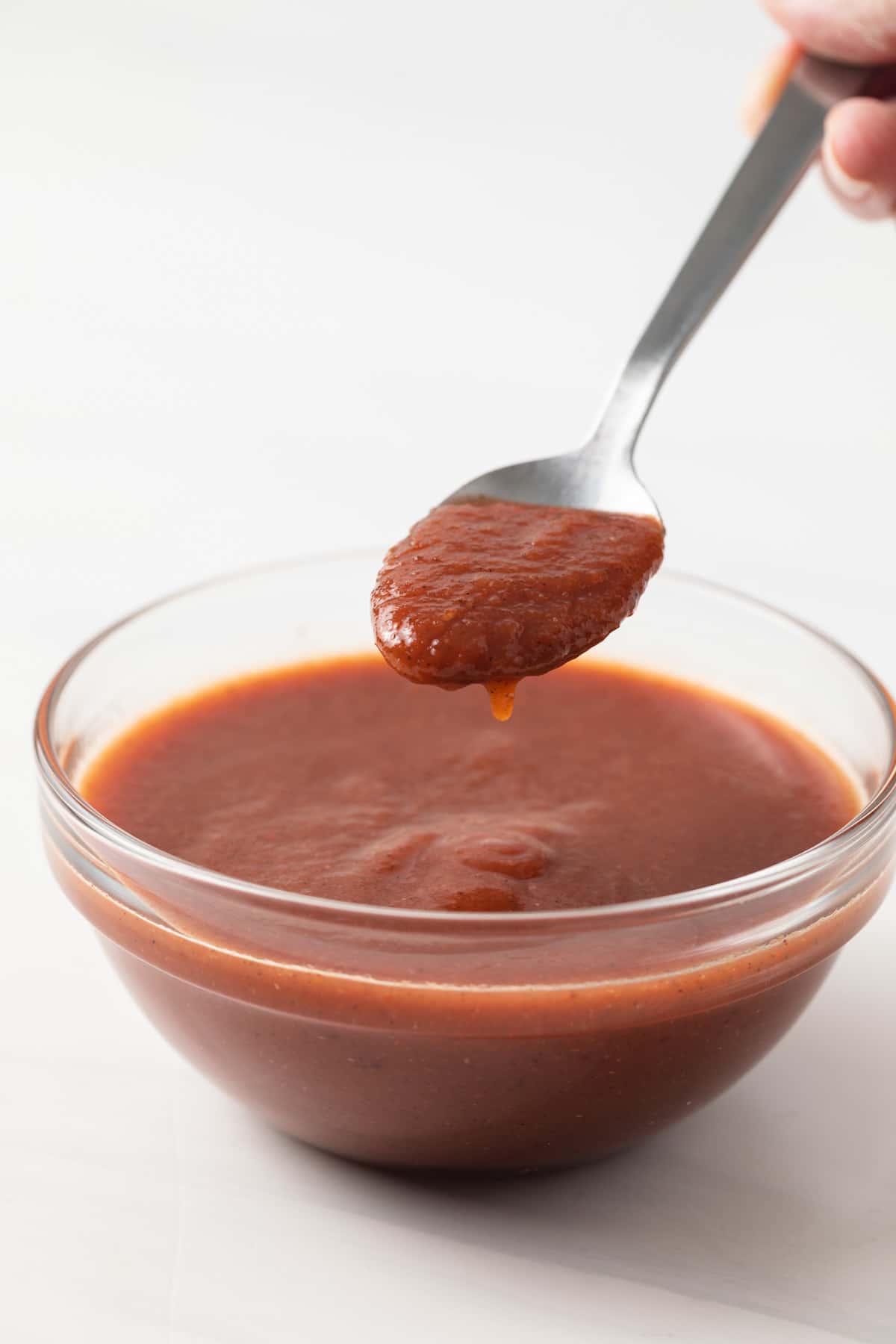 Chili sauce on spoon over glass bowl.