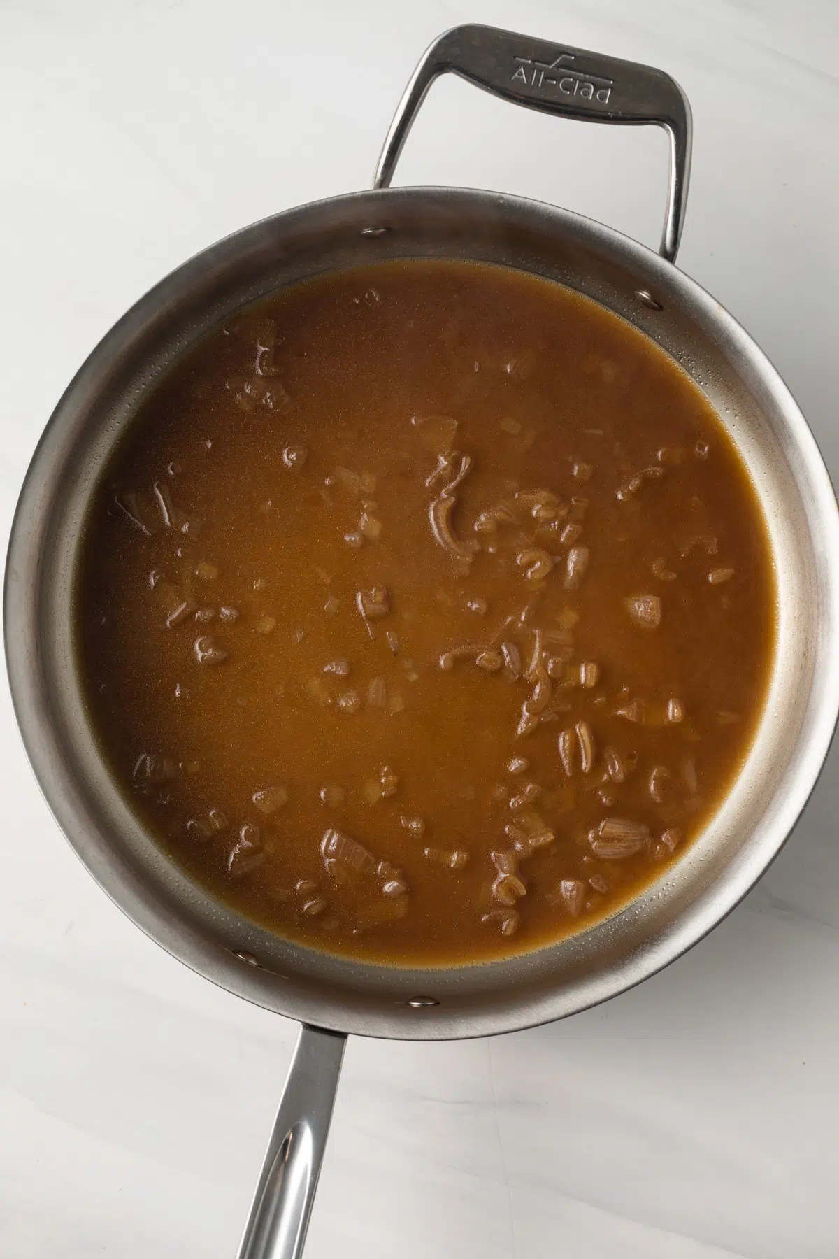 Beef broth in a skillet with shallots.