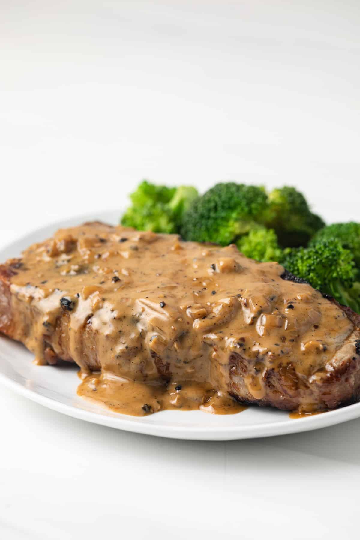 Side view of creamy peppercorn sauce over a steak.