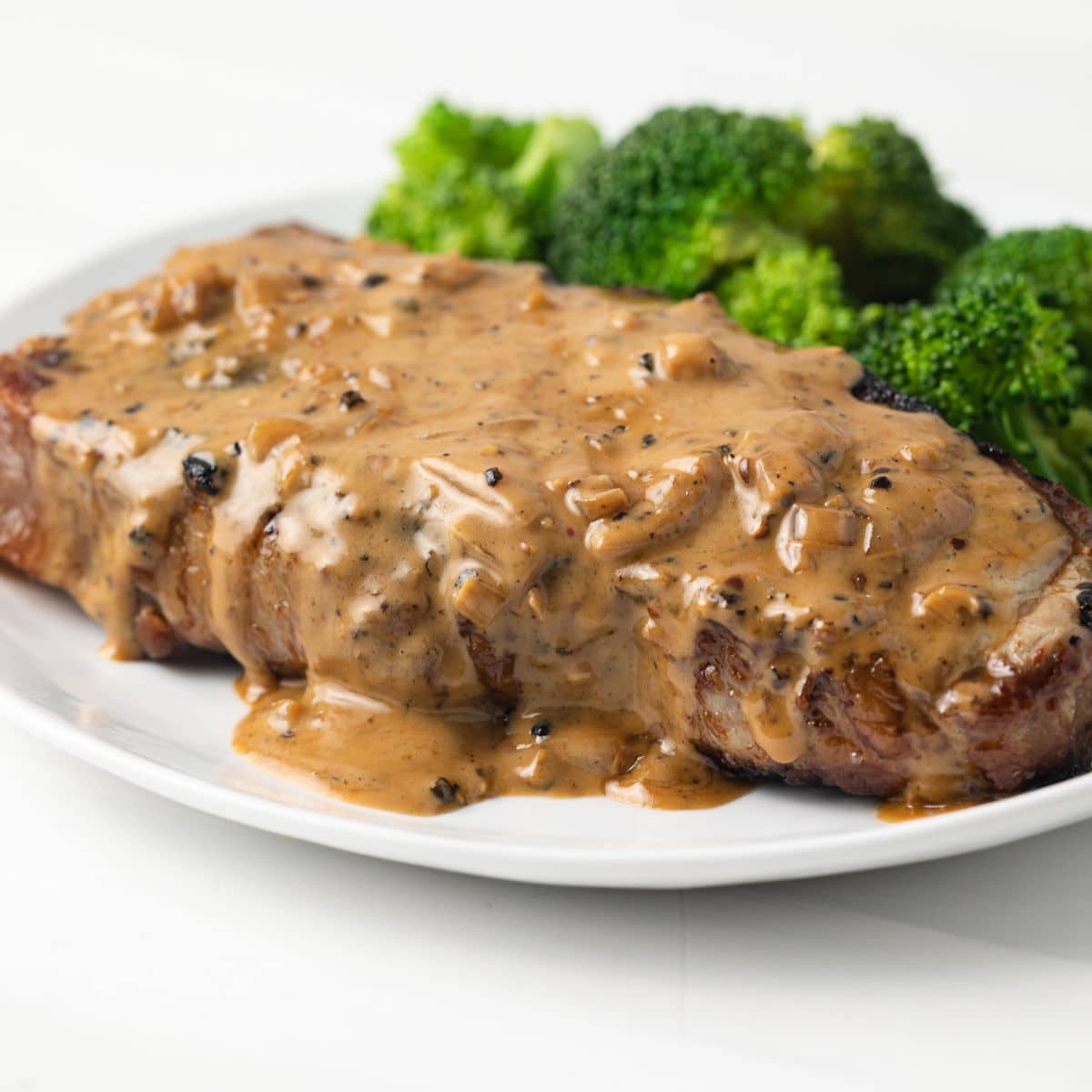 Side view of creamy peppercorn sauce over a steak.