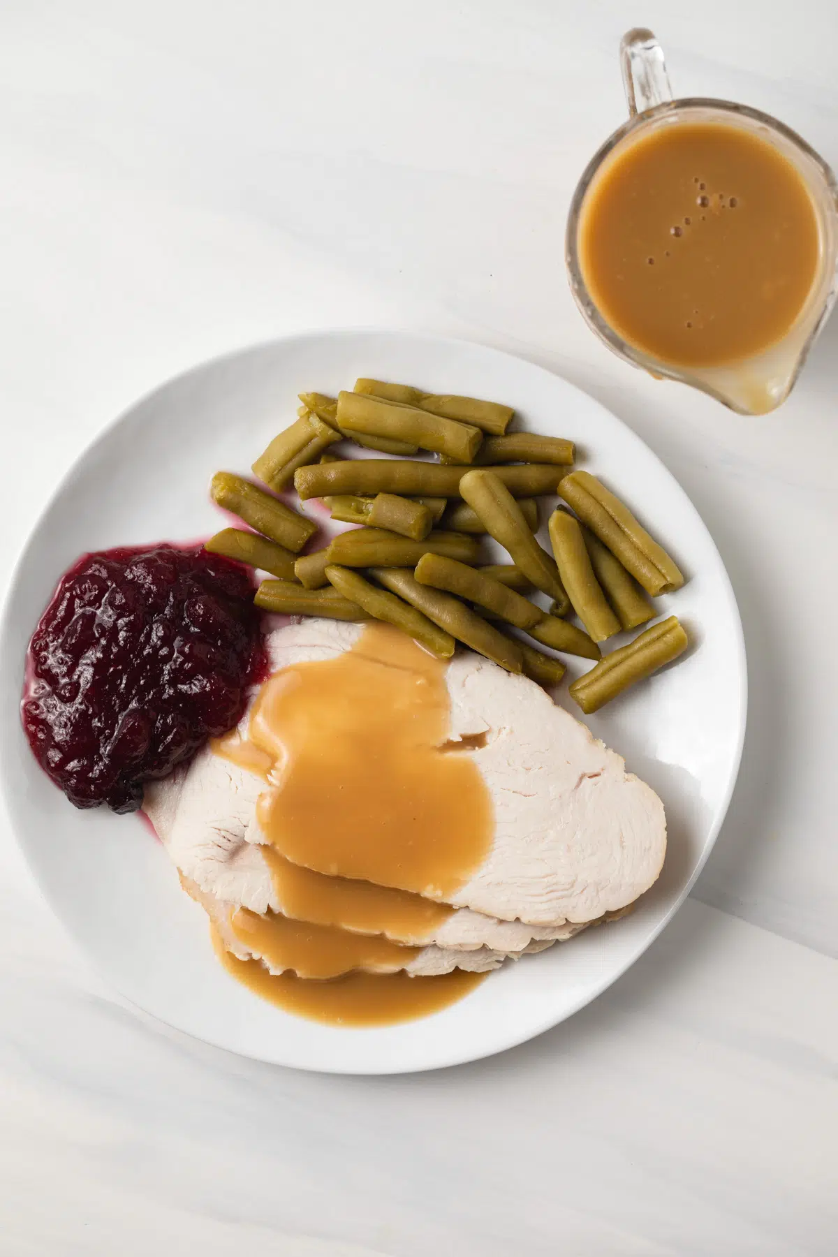 Overhead of turkey with turkey gravy on plate beside green beans and cranberry sauce.