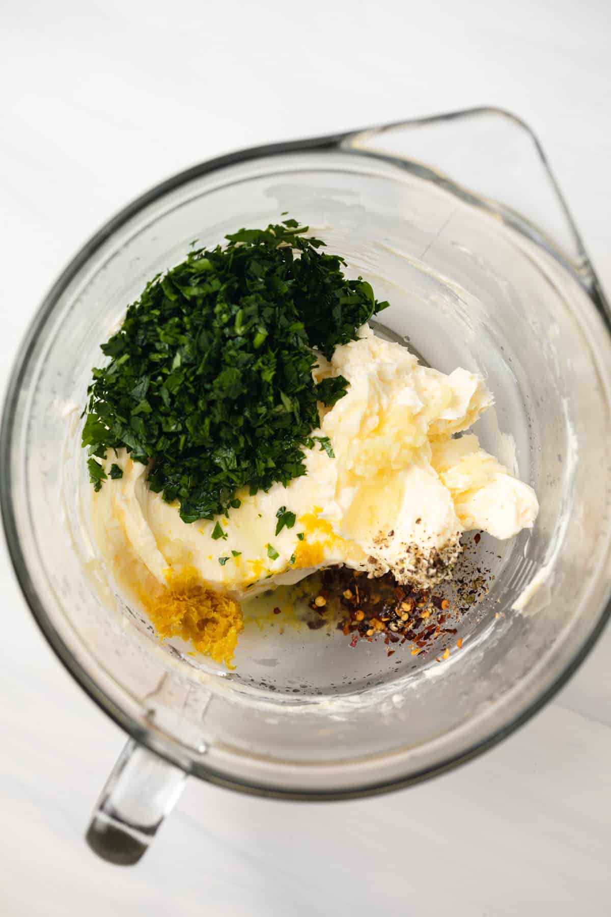 Butter with parsley, pepper, lemon zest and garlic in a glass mixing bowl.