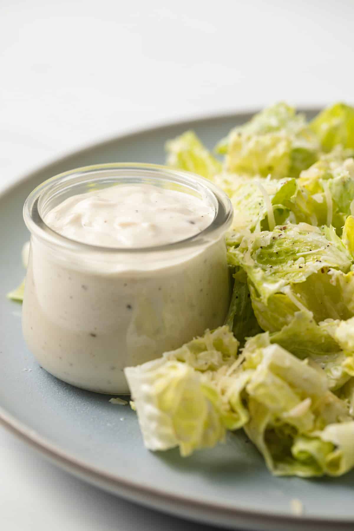 Side view of caesar dressing in a glass ramekin.