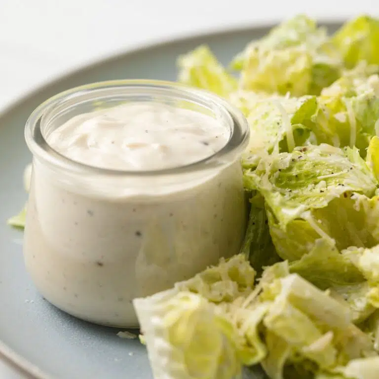 Side view of caesar dressing in a glass ramekin.