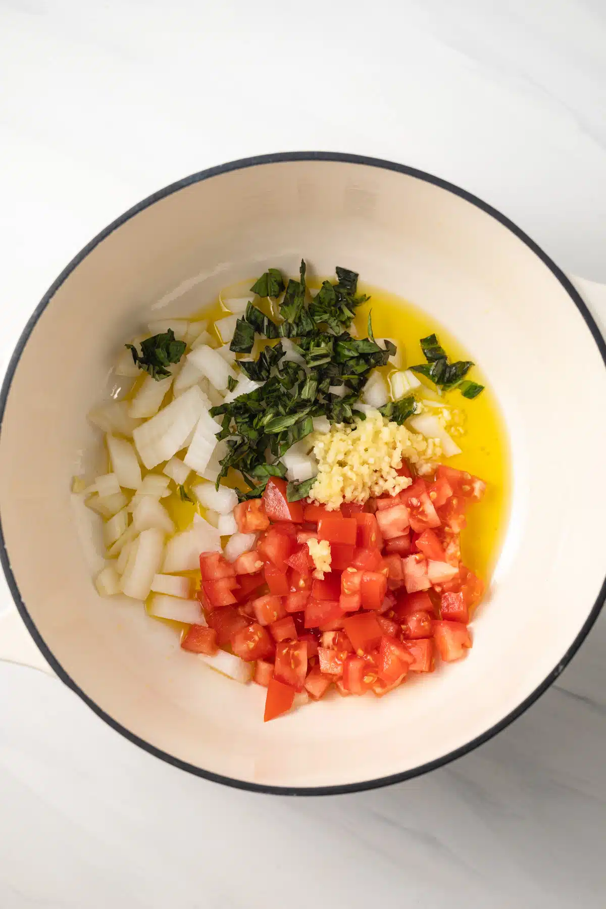 Onion, tomato, garlic, and basil in saucepan.