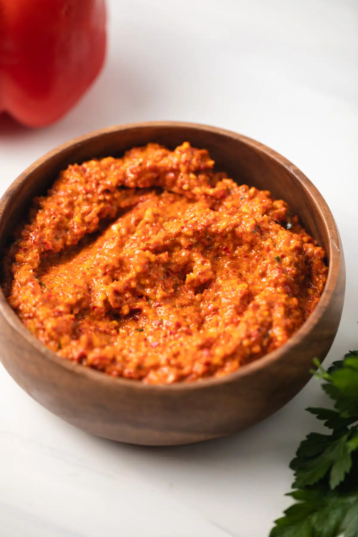 Side view of red pepper romesco in a brown bowl.