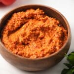 Side view of red pepper romesco in a brown bowl.