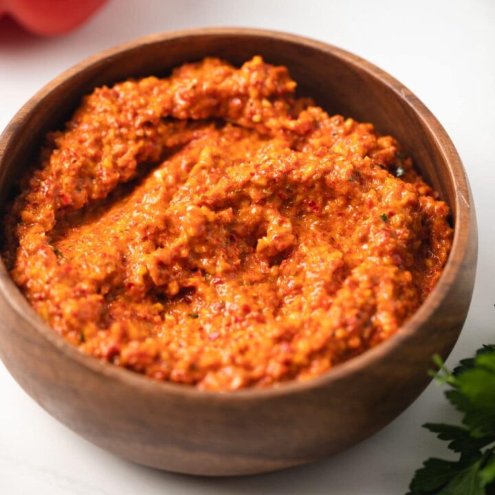 Side view of red pepper romesco in a brown bowl.