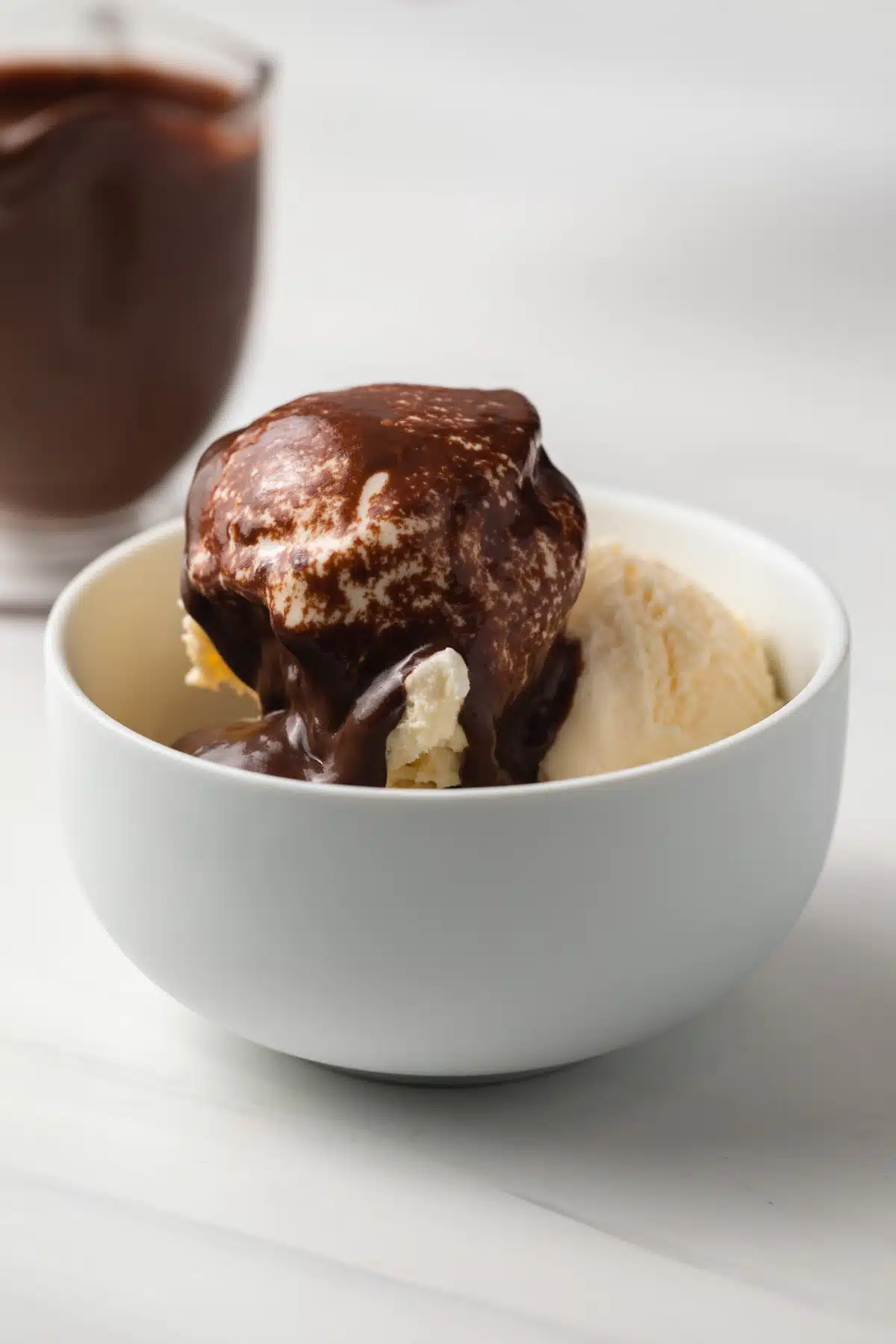 Chocolate sauce over vanilla ice cream in white bowl.