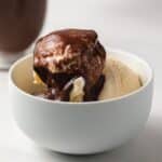 Chocolate sauce over vanilla ice cream in white bowl.