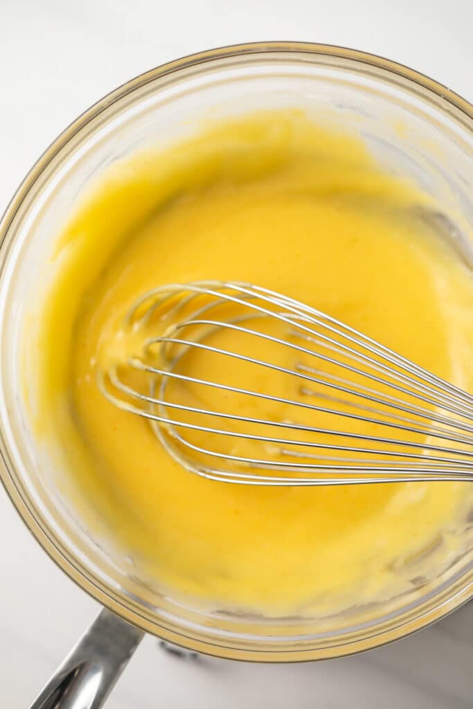 Hollandaise sauce in glass bowl with whisk.