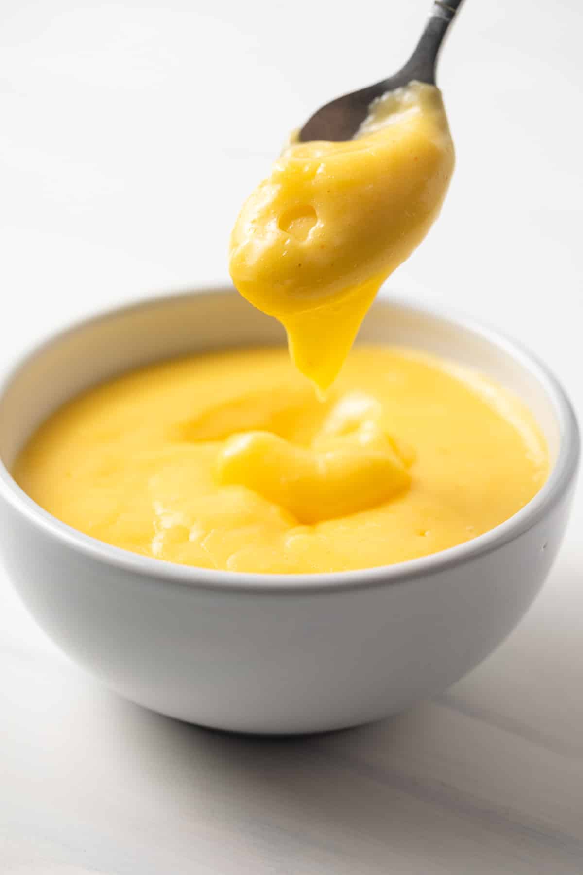 Hollandaise sauce in a bowl with spoon taking some out.