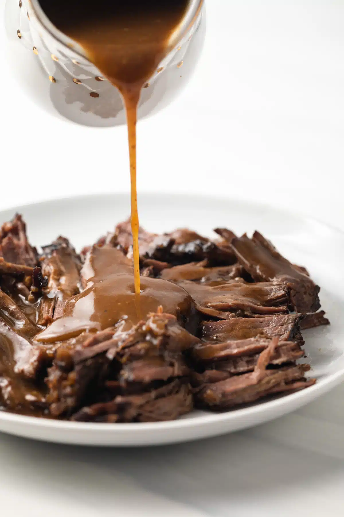 Pot roast gravy being poured over shredded roast.