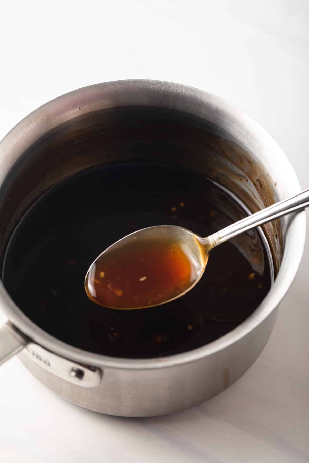 Homemade teriyaki sauce in a saucepan with a spoon.