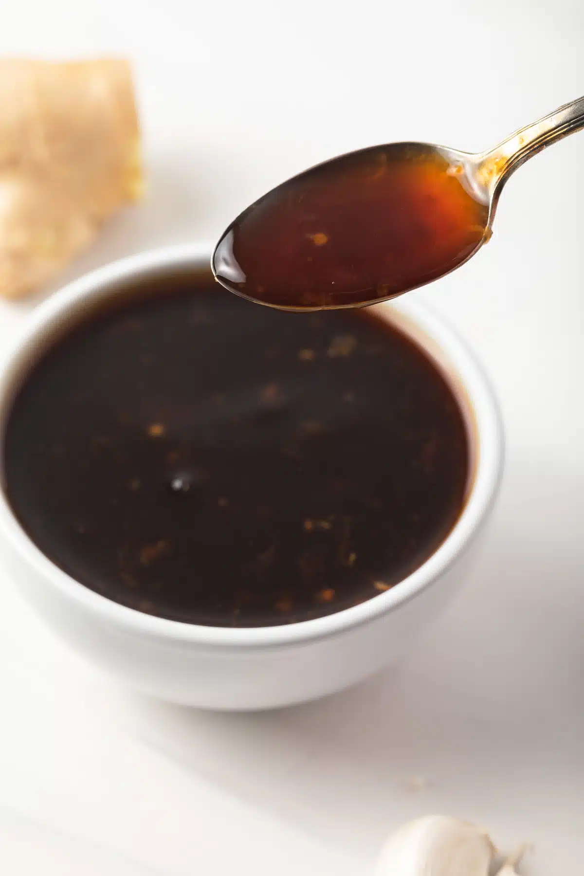 A spoon taking teriyaki sauce out of a white bowl.
