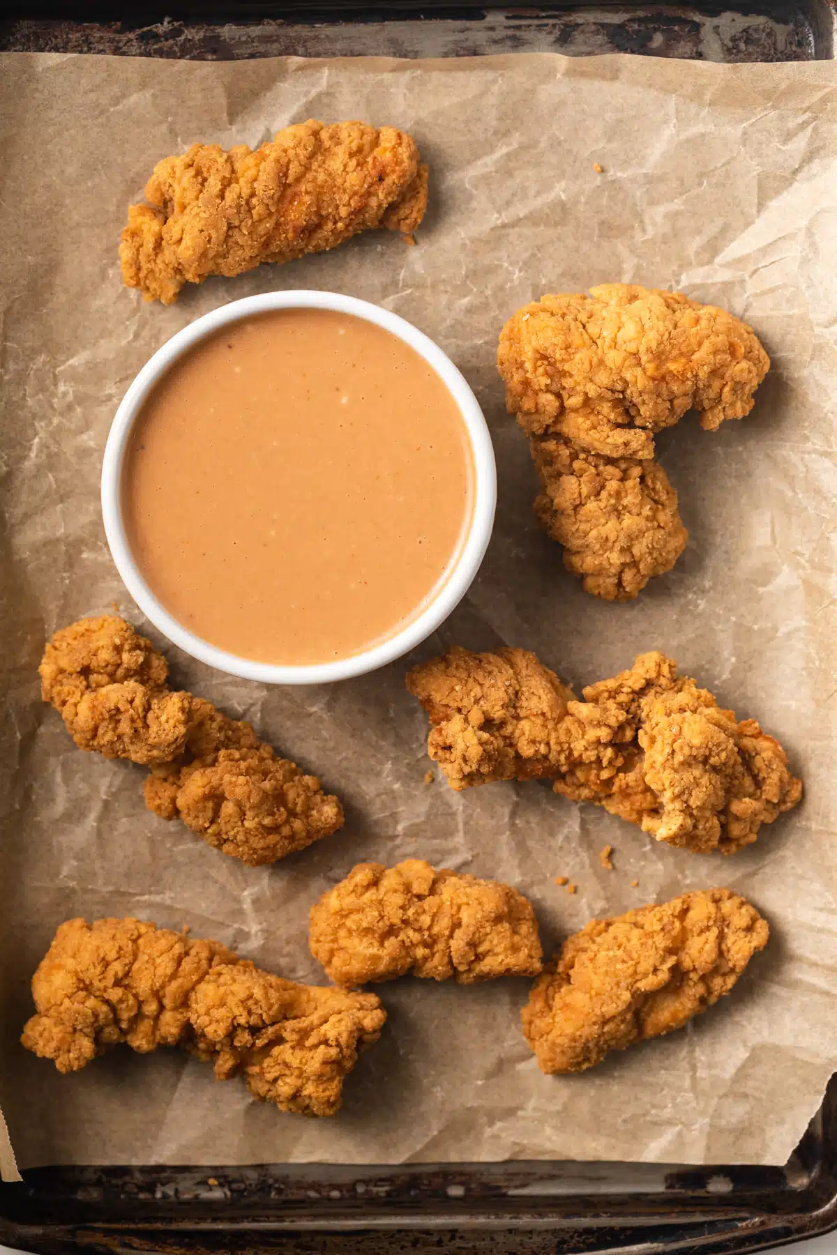 Chicken nugget dipping sauce in white bowl with chicken nuggets scattered around.