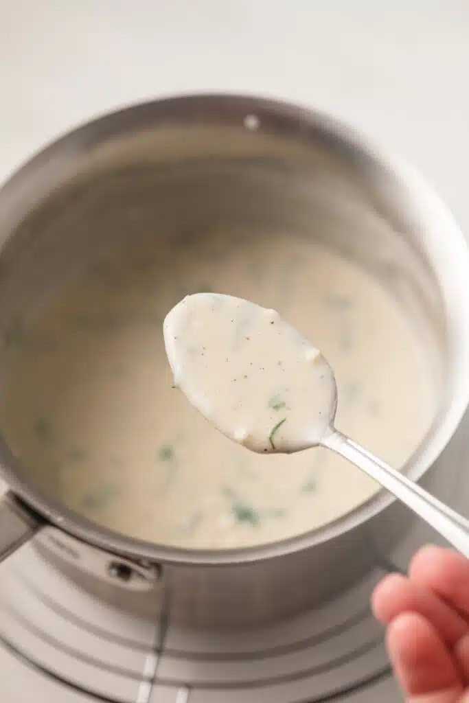 White garlic sauce on a spoon over a saucepan.