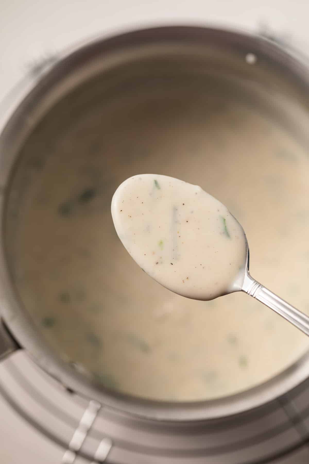 White garlic sauce on a spoon over a saucepan.