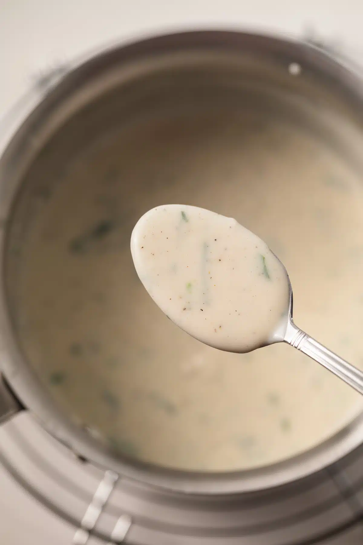 White garlic sauce on a spoon over a saucepan.