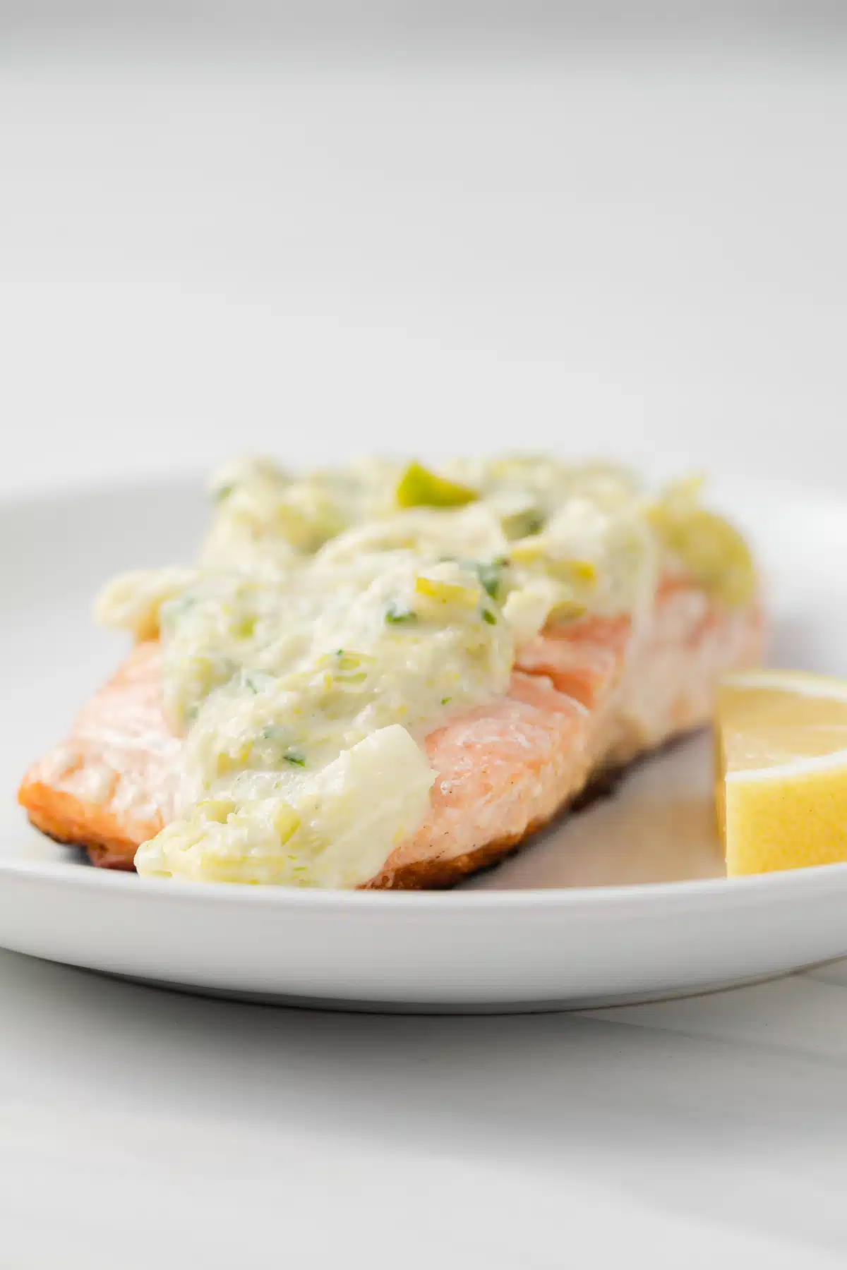 Creamy leek sauce over salmon with lemon wedge.