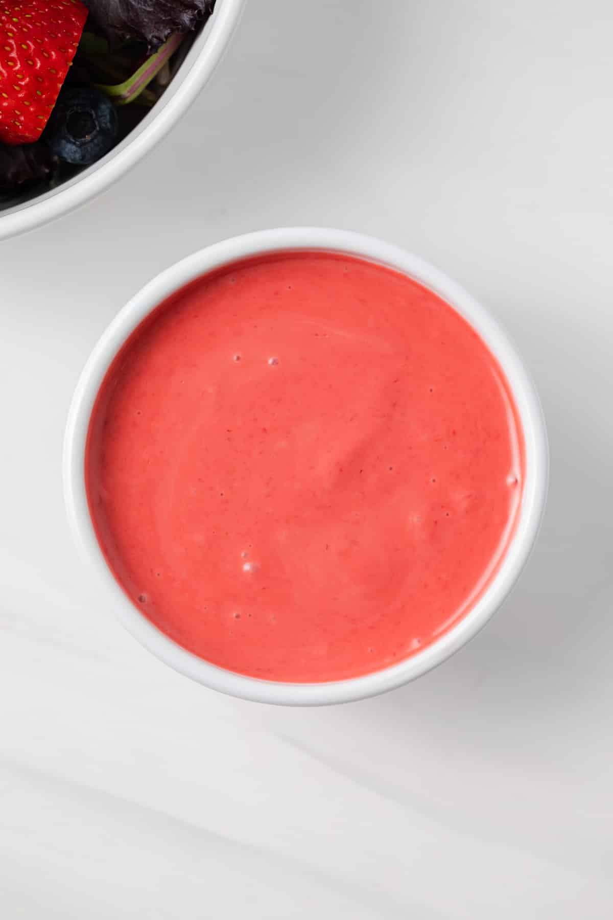 Overhead of raspberry vinaigrette in white bowl.