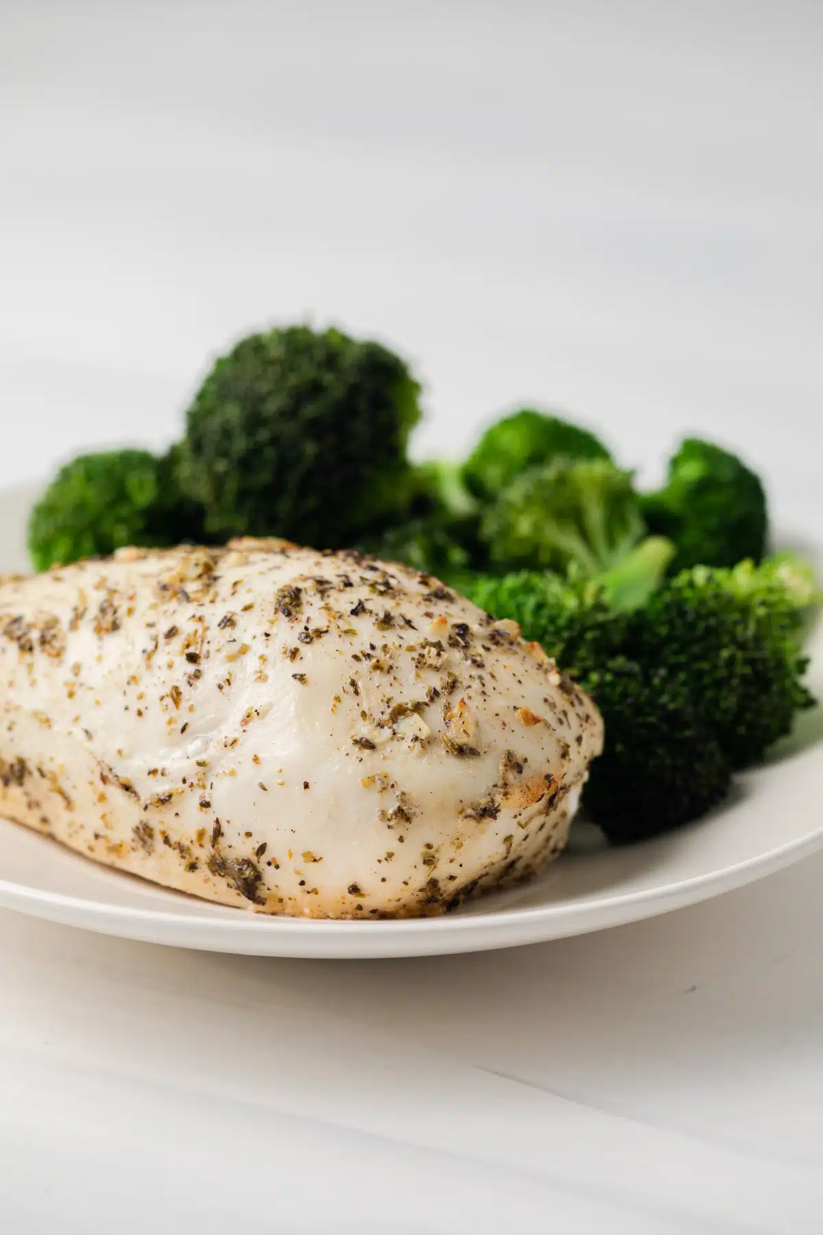 Side view of Italian dressing chicken marinade coated chicken on a plate with broccoli.