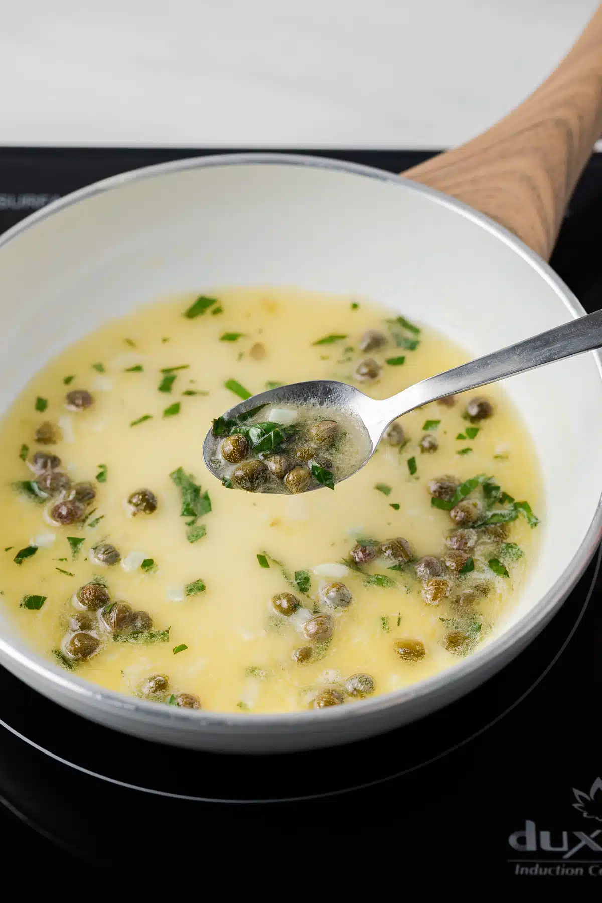 Lemon caper sauce in skillet with a spoon taking some out.